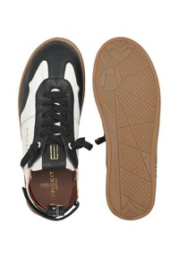 Le scarpe sportive in bianco e nero presentano una tomaia in pelle, punta rotonda, lacci neri e una suola in gomma marrone con una superficie grip a motivo testurizzato.
