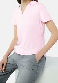 Camisa polo rosa claro con cuello en V y mangas cortas, hecha de una tela suave. Llevada con unos jeans sueltos de color gris claro.