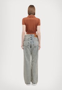 Brun kortermet polo skjorte parret med høy midje, vide lyseblå jeans. Har en lærlapp på midjebåndet og enkle sømmer.