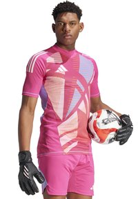 Maillot de sport rose avec des motifs géométriques, à manches courtes et col montant. Gants de gardien de but noirs. Tenant un ballon de football avec des accents rouges.