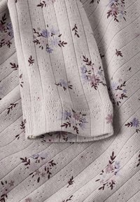 Dzianina w jasnoszarym kolorze z pionowymi paskami; ozdobiona małymi kwiatowymi wzorami w kolorze fioletowym i bordowym. Miękka w dotyku z prążkowanymi krawędziami.