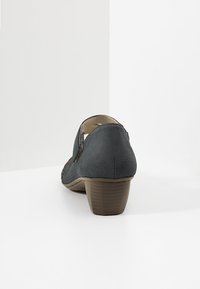 Scarpa con tacco grigio realizzata in tessuto testurizzato con dettagli ritagliati. Presenta un tacco a blocco basso e una punta arrotondata.