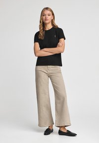 Svart bomullströja med ribbad halsringning, tillsammans med ljusbeige vida byxor och svarta ballerina skor. Enkelt mönster, inga synliga mönster.