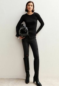 Suéter negro de manga larga con textura acanalada, jeans negros rasgados y botas de cuero negro hasta la rodilla. Los accesorios incluyen un bolso negro y pendientes de aro de plata.
