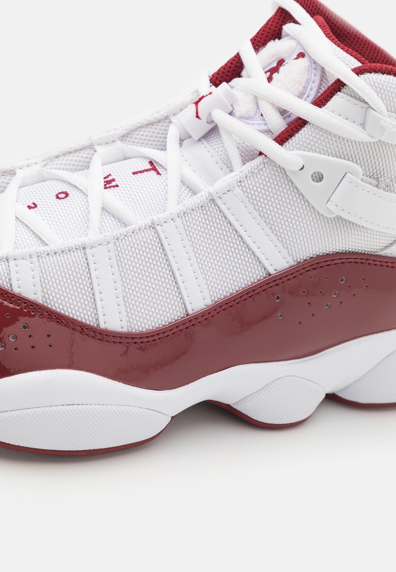 Chaussure de sport blanche et rouge avec une tige en mesh, des accents synthétiques rouges brillants, une semelle blanche texturée et des détails rouges sur la languette.
