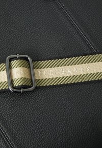 Zwart gestructureerd leer met een gevlochten khaki riem. Een zilveren rechthoekige gespsluiting benadrukt de riem, met "TED BAKER" in lichtbruin.