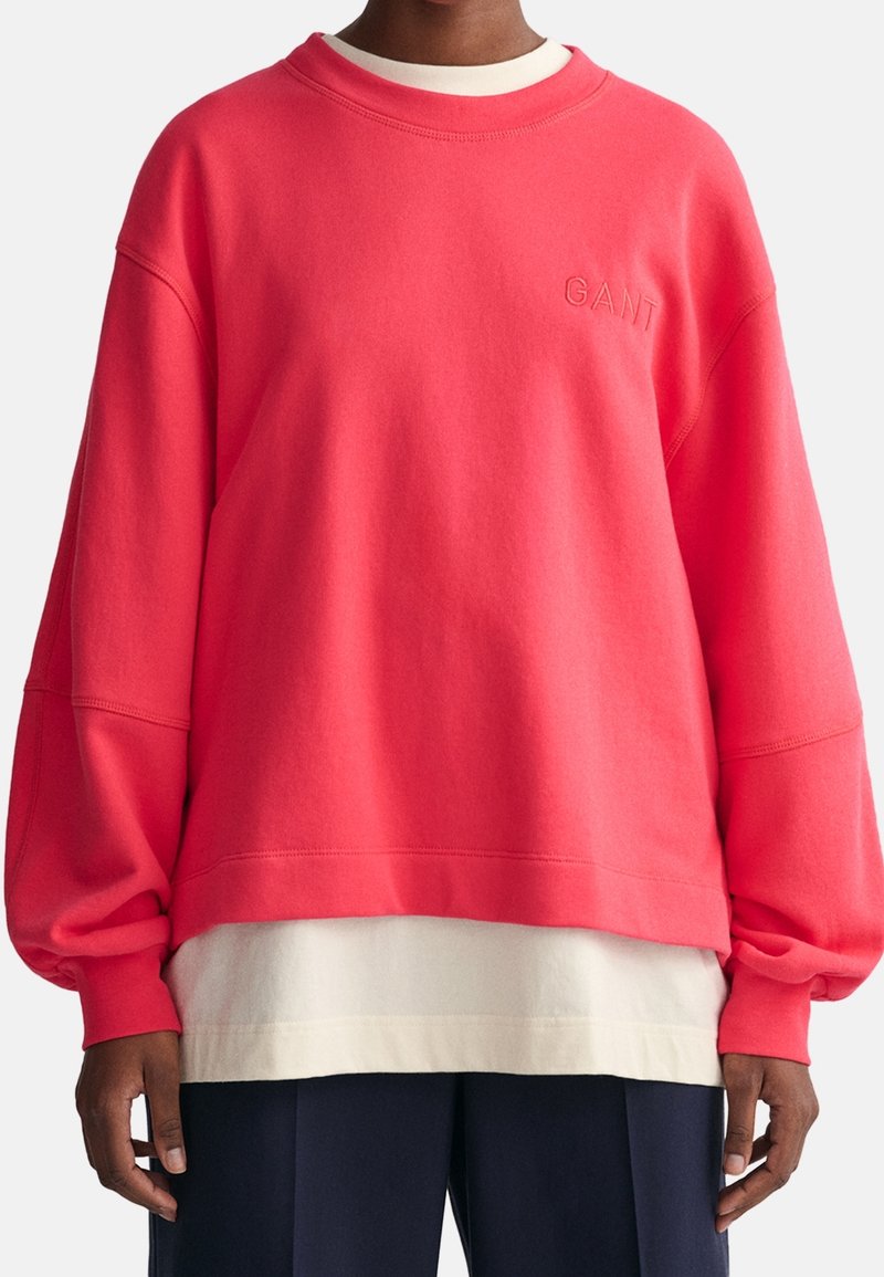 Koronowy, oversized sweatshirt z prążkowanym dekoltem w okrągłym kształcie i opadającymi ramionami. Posiada haftowane logo "GANT". Warstwowy na białej bluzce.