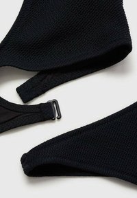 Čierny bikiny top a remienok s textúrovanou tkaninou, nastaviteľným uzáverom a hladkým podšívaním. Žiadne vzory ani ďalšie farby nie sú prítomné.