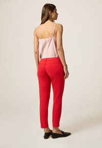 Pantaloni aderenti rossi con una consistenza liscia, abbinati a un top in satin rosa chiaro con spalline sottili. Ballerine nere completano il look.