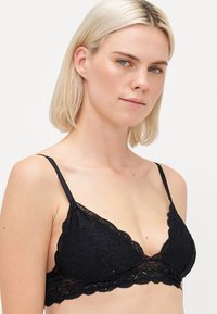 Black lace bra featuring a triangular shape, adjustable straps, scalloped trim, and intricate floral patterns throughout.