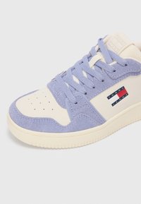 Adidași din suede mov și piele crem cu vârf perforat, ș nur flat și un logo pe lateral în dungi roșii, albe și albastre.