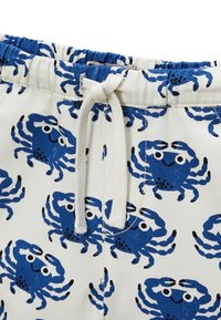 Shorts blancs avec un imprimé de crabes bleus, dotés d'une taille élastique et d'un cordon de serrage blanc. Le motif se compose de crabes bleus stylisés avec des visages souriants.