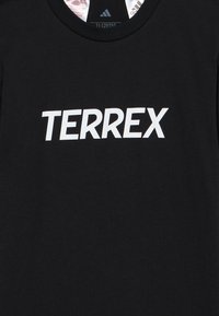 Μαύρο βαμβακερό κοντομάνικο με μεγάλο λευκό λογότυπο "TERREX" στο στήθος. Σχέδιο με στρογγυλή λαιμόκοψη, μαλακή υφή, χωρίς επιπλέον σχέδια ή διακοσμήσεις.