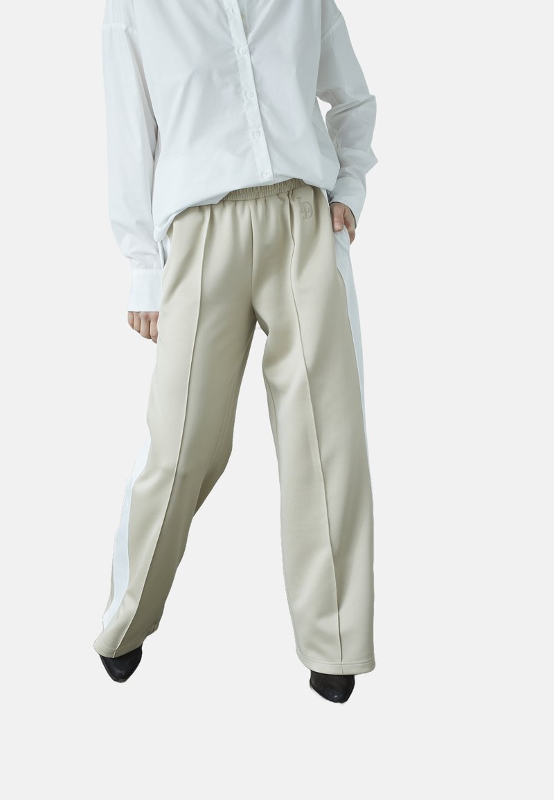 Beige polyester bukser med en løs pasform, der har hvide sidelængder og et struktureret taljebånd, kombineret med en hvid skjorte med knapper.