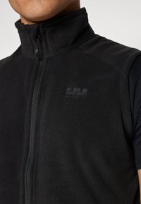 Gilet en polaire noir avec col montant et fermeture éclair, arborant un logo discret sur la poitrine et une texture lisse.