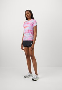 Short-sleeve athletic shirt in pink with multicolor abstract pattern. Paired with black shorts and gray athletic shoes with reflective accents.