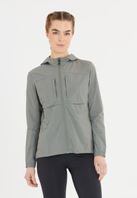 Lätt, grå zip-jacka med huva, som har två bröstfickor och elastiska manschetter för en figurnära passform och känsla.