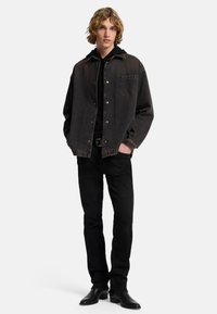 Giacca in denim nera con bottoni metallici, tasca sul petto e colletto a contrasto, abbinata a jeans neri aderenti e stivaletti neri.