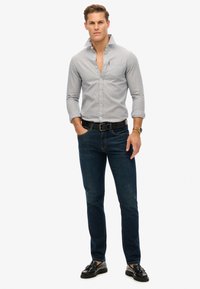 Camicia a righe grigie e bianche con bottoni abbinata a jeans blu scuro e scarpe nere. Presenta un colletto e una vestibilità casual.