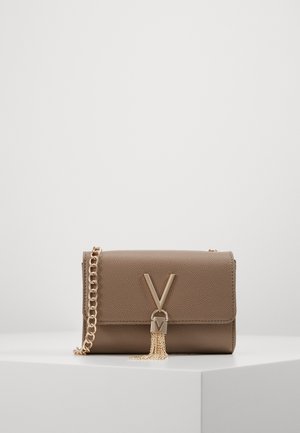 Taupekleurige leren crossbodytas met gouden kettingriem, V-vormige gouden sluiting en gouden kwastaccent op een witte ondergrond.