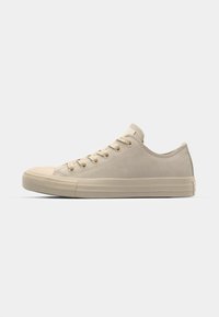 Zapatillas de lona beige de corte bajo con puntera redonda, cierre de cordones en la parte frontal y acabado de ante texturizado. Presenta suela de goma y acentos de marca mínimos.