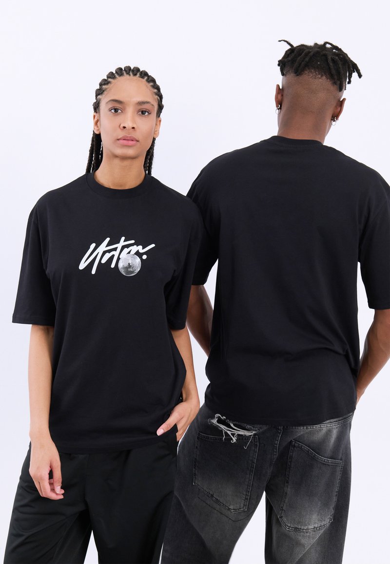 Sort bomulds t-shirt med korte ærmer, prydet med et hvidt grafisk design og måne detalje på forsiden. Bæres med sorte bukser og slidte jeans.