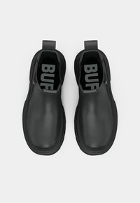 Čierne nazúvacie topánky s hladkým matným povrchom, so zaoblenou špicou a výraznými pútkami na obúvanie. Logo viditeľné na stielkach.