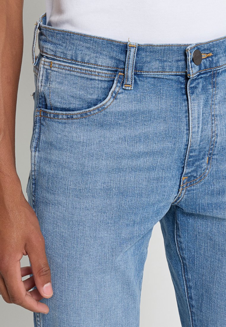 Jasnoniebieskie dżinsy w prostym kroju, z przednimi kieszeniami, metalowym guzikiem i kontrastującymi szwami.