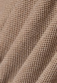 Gestructureerde stof in een lichte beige kleur, met een geweven patroon met zichtbare kleine gaatjes en een zachte afwerking, in vouwen gedrapeerd.