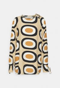 Blusa de manga longa em tecido bege com um grande padrão circular em preto, branco e castanho. Laços nas mangas adicionam detalhe.
