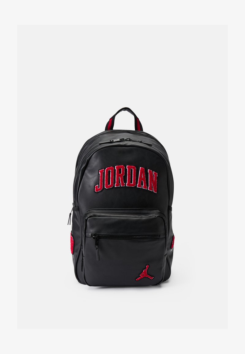 Crna ruksak ima crveno vezeni logo "JORDAN", džepove sa patentnim zatvaračem i crveni akcent sa strane s crnim Jumpman logom.