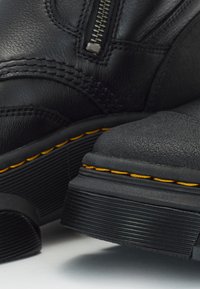 Bottes en cuir noir avec une finition texturée, dotées d'une fermeture éclair sur le côté, de coutures jaunes et d'une semelle en caoutchouc durable.