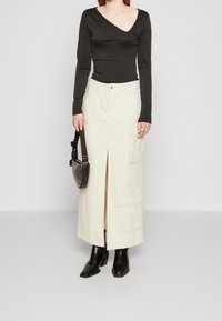 Černý žebrovaný top s dlouhým rukávem a výstřihem do V; krémová cargo sukně s předním rozparkem a bočními kapsami; černé kotníkové boty; malá kabelka.