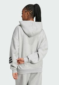 Siva dukserica s kapuljačom i opuštenim krojem. Ima jednostavan dizajn, rebraste manžetne i tri crne pruge na lijevom rukavu.