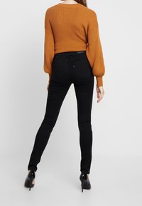 Jeans skinnies negros combinados con un suéter naranja acanalado que presenta mangas abullonadas; el suéter tiene un escote redondo y una tela texturizada.