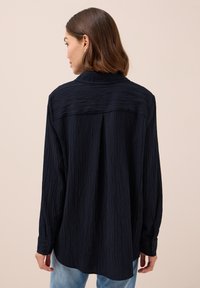 Marineblaues Langarmhemd aus strukturierter, zerknitterter Stoffqualität, mit Rückenpasse, Knopfmanschetten und einer lockeren Passform.