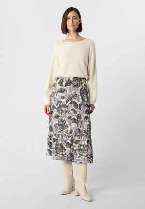 Knit cream sweater paired with a patterned, tiered maxi skirt in pastel tones featuring floral designs, worn with knee-high beige boots.