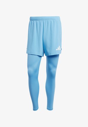 Hellblaue Sportshorts mit einem elastischen Bund, über passgenauen Leggings in passendem Farbton getragen. Die Shorts sind mit weißen Logo-Akzenten versehen.