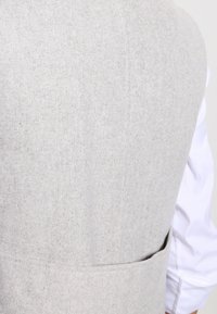 Grå ullväst med en enkel textur, något figursydd form och en bakficka. Minimalistisk design utan synliga detaljer i metall.