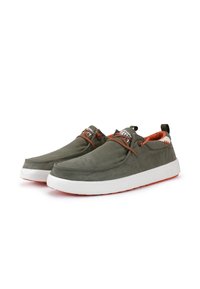 Des chaussures en toile vertes avec des semelles blanches, des accents orange et un design sans lacets. Texture lisse avec des coutures discrètes et des détails de marque.