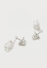 Ζεύγος ασημένιων σκουλαρικιών καρφίτσας με περίπλοκα κυκλικά και γραμμικά σχέδια σε απλό λευκό φόντο.