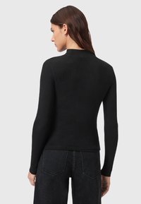 Maglietta nera a maniche lunghe con una texture a coste, colletto alto e design aderente. Abbinata a jeans in denim scuro, mostra una silhouette elegante e minimalista.