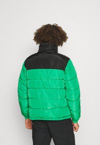Giacca imbottita con un corpo verde lucido e una parte superiore nera. Presenta una texture trapuntata e un alto colletto per il calore.