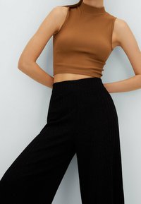 Bruine geribbelde crop top met hoge hals, gecombineerd met zwarte wijde broek met een gestructureerd, verticaal streepjespatroon.