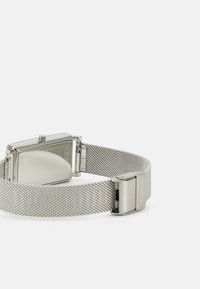 Rektangulär silverfärgad klocka i rostfritt stål med mesharmband, som har en slät yta och en minimalistisk design. Justerbar spänne.