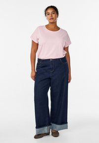 Camiseta de manga corta de color rosa claro combinada con vaqueros de corte holgado en azul oscuro, con puños doblados y cierre de botones. Diseño sencillo y casual.