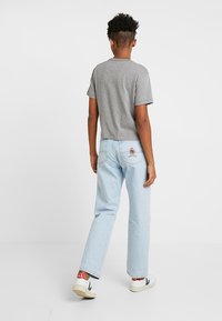 Grå t-shirt med kort ärm i kombination med ljusblå raka jeans, med en broderad patch på bakfickan och vita sneakers.