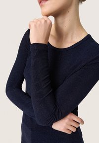 Navy blue long-sleeve top made of shimmering fabric, featuring a rounded neckline and fitted design. Smooth texture with subtle sparkle accents.