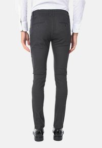 Pantaloni slim-fit neri, texturizzati, con vita a media altezza, dotati di tasche posteriori e una finitura liscia, abbinati a scarpe nere lucide.