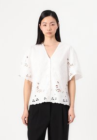 White, short-sleeve blouse featuring intricate floral embroidery and cut-out patterns along the hem, with a V-neckline and button closure.